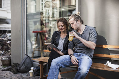 Couple using digital tablet together on sidewalk bench