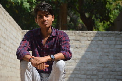 Young man looking away while sitting on wall