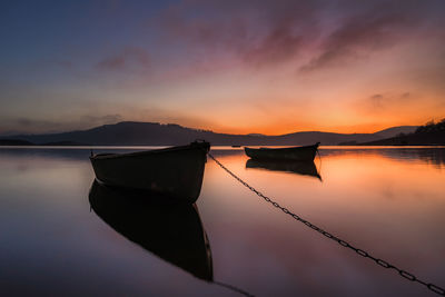 Sailboats moored on lake against sky during sunset