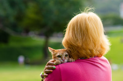 Domestic cat with scared face carried by teenager owner when take out to travel at the park.