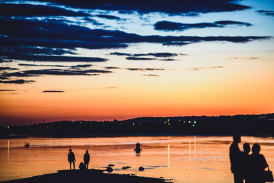 Silhouette people at beach against sky during sunset