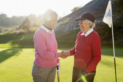Happy senior female golfers shaking hands on golf course