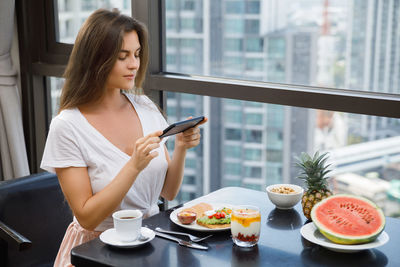 Young woman using phone while sitting on table