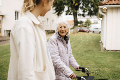 Smiling senior woman looking at female nurse while walking in front yard