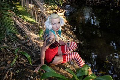 Portrait of female model sitting by pond on field
