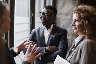 Businessman with arms crossed by businesswoman looking at male delegate explaining during meeting in conference center