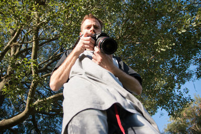 Low angle view of man holding camera against trees