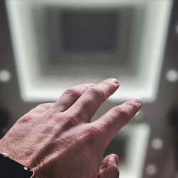 Cropped hand of man gesturing against illuminated wall