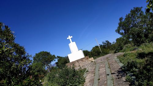 Low angle view of cross amidst trees against blue sky