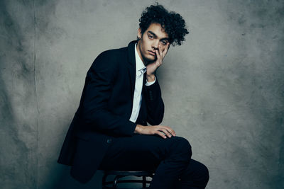 Young man sitting on chair against wall