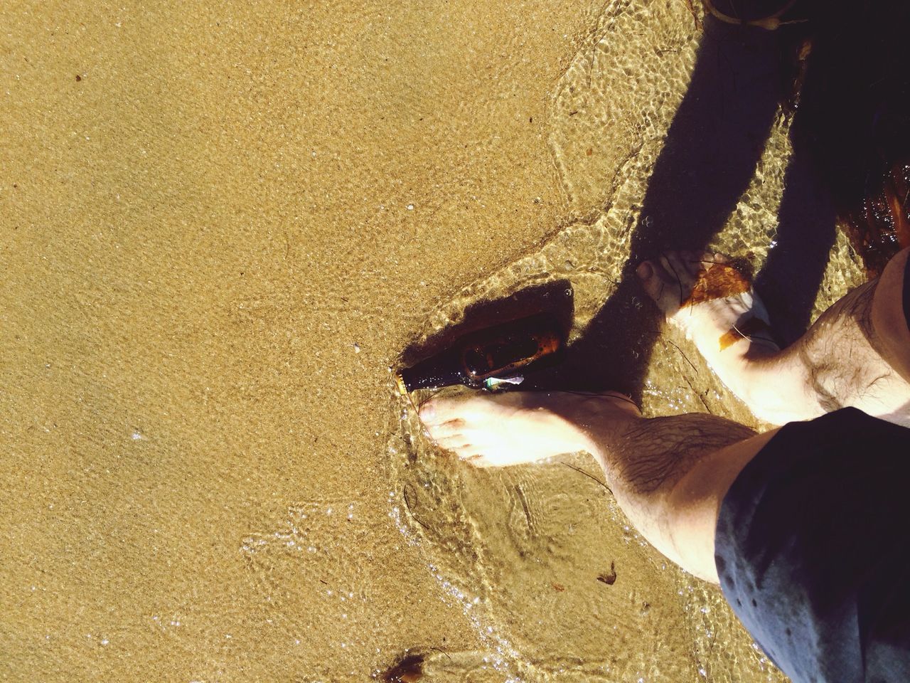 low section, sand, beach, person, lifestyles, leisure activity, men, personal perspective, high angle view, human foot, unrecognizable person, shore, sunlight, standing, part of, shadow