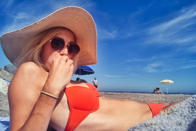 Midsection of woman holding hat at beach against sky