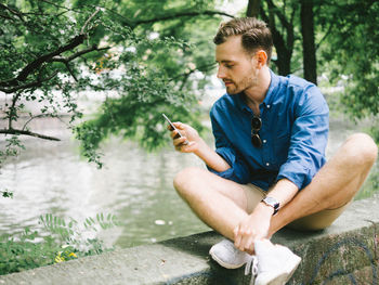 Young man using smart phone while sitting by tree