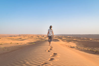 Rear view full length of woman walking at desert against clear sky