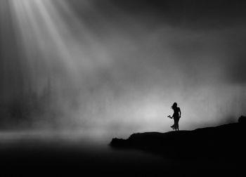 Silhouette woman standing on land against sky during foggy weather