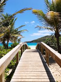 Wooden footbridge leading to palm trees against sky