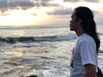 Side view of man looking at sea shore against sunset sky