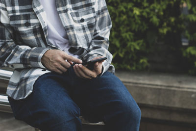 Midsection of man using mobile phone while sitting on seat