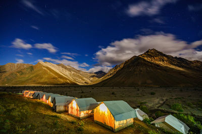 Illuminated tents by mountains against sky at dusk