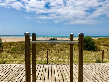 Wooden railing on beach against sky