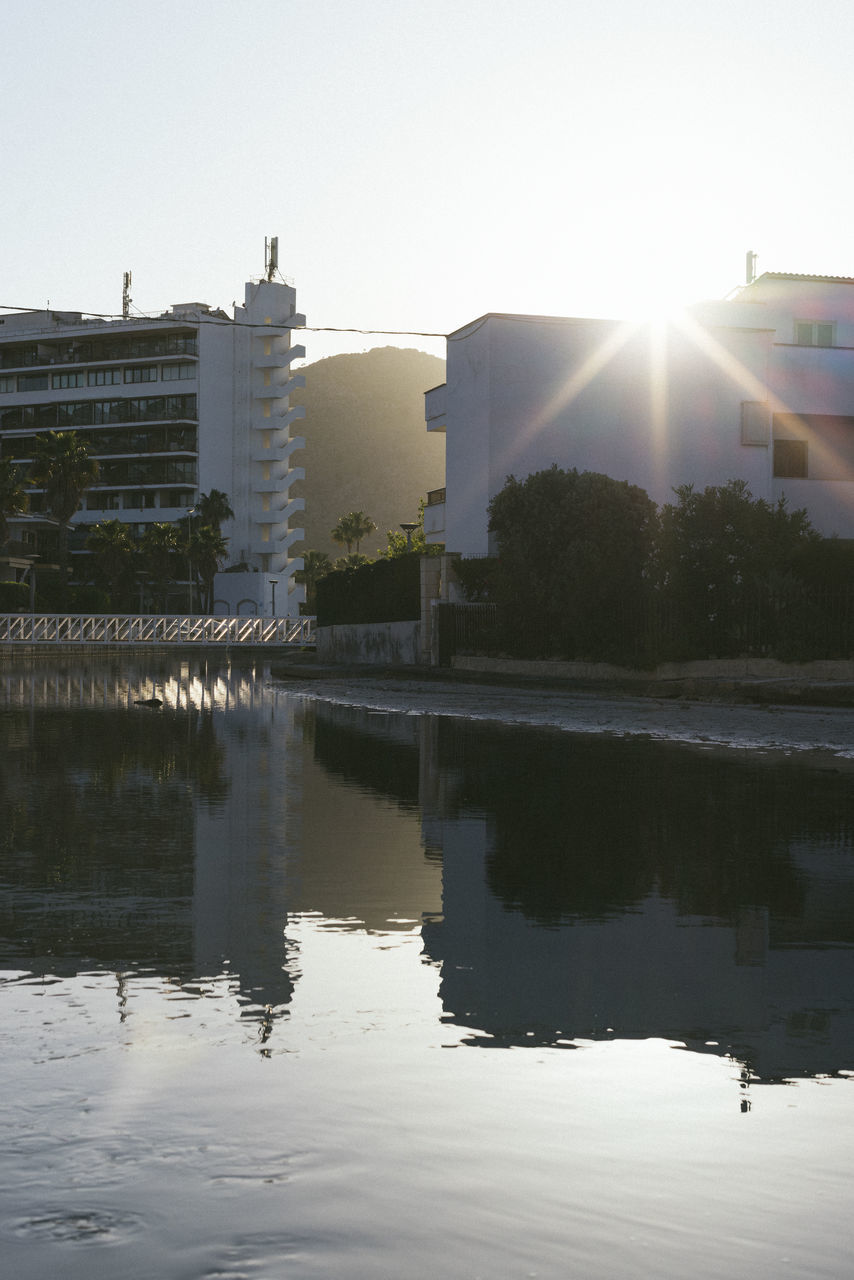 reflection, water, architecture, built structure, sky, building exterior, nature, building, morning, city, sun, sunlight, no people, lake, outdoors, lens flare, tree, day, environment, travel destinations