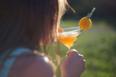 Woman sipping orange peach cocktail in glass with ice cubes and straw