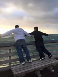 Rear view of men standing on railing against sky