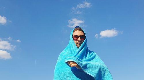 Low angle view of man wrapped in towel against blue sky on sunny day