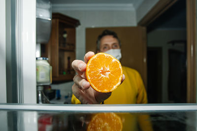 Middle-aged man with mask at the empty fridge with half an orange