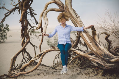 Full length of young woman standing on tree trunk at beach