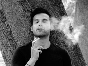 Young man smoking on tree trunk