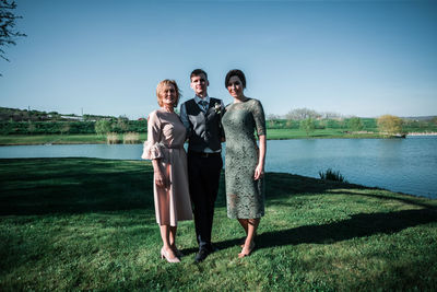 Full length of friends standing by lake against sky