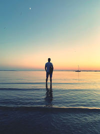 Rear view of man standing on beach against sky during sunset