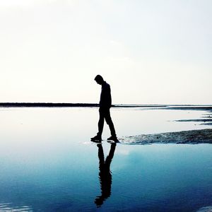 Silhouette man standing in sea against sky