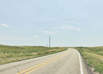 Road by electricity pylon against sky
