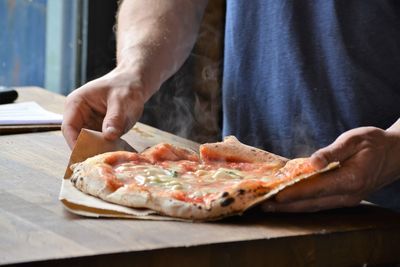 Midsection of man holding pizza at table