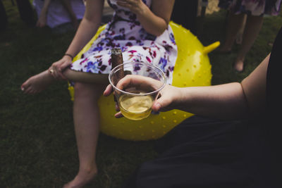 Cropped image of woman holding drink in glass with cigar while sitting outdoors