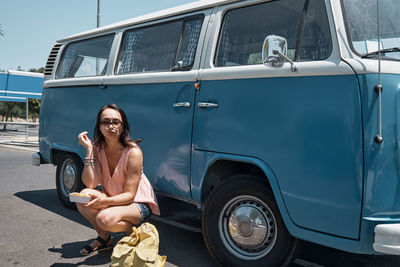 Young woman eating unhealthy fast food near a camper van in urban parking. traveling and summertime. 