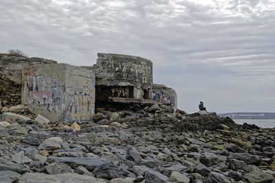 Man standing on rock by sea against sky