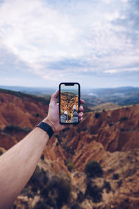 Man photographing with mobile phone against sky