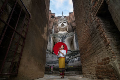 Woman with umbrella standing against buddha statue and sky