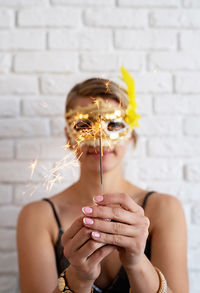 Close-up of woman holding sparkler against wall