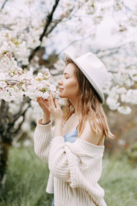 Gentle girl in a dress and a fashionable hat is walking enjoying the smell of blooming flowers 