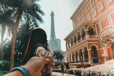 Cropped image of man holding girlfriend hand against building