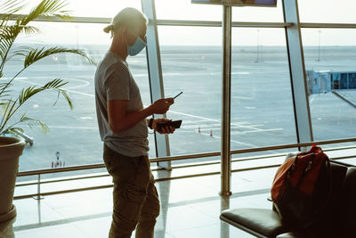 Man with power bank at the airport, charging phone passenger in mask traveling during covid. 