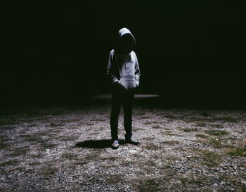 Man wearing hooded sweatshirt standing on illuminated ground