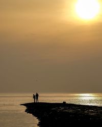 Silhouette people on beach against sky during sunset