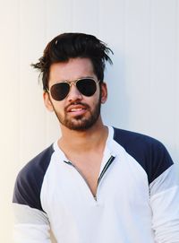 Portrait of young man wearing sunglasses standing against wall