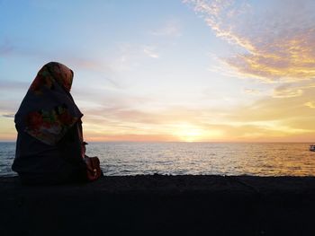 Rear view of woman wearing hijab looking at sea against sky during sunset