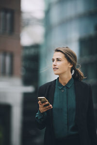 Young man looking at camera while standing on mobile phone